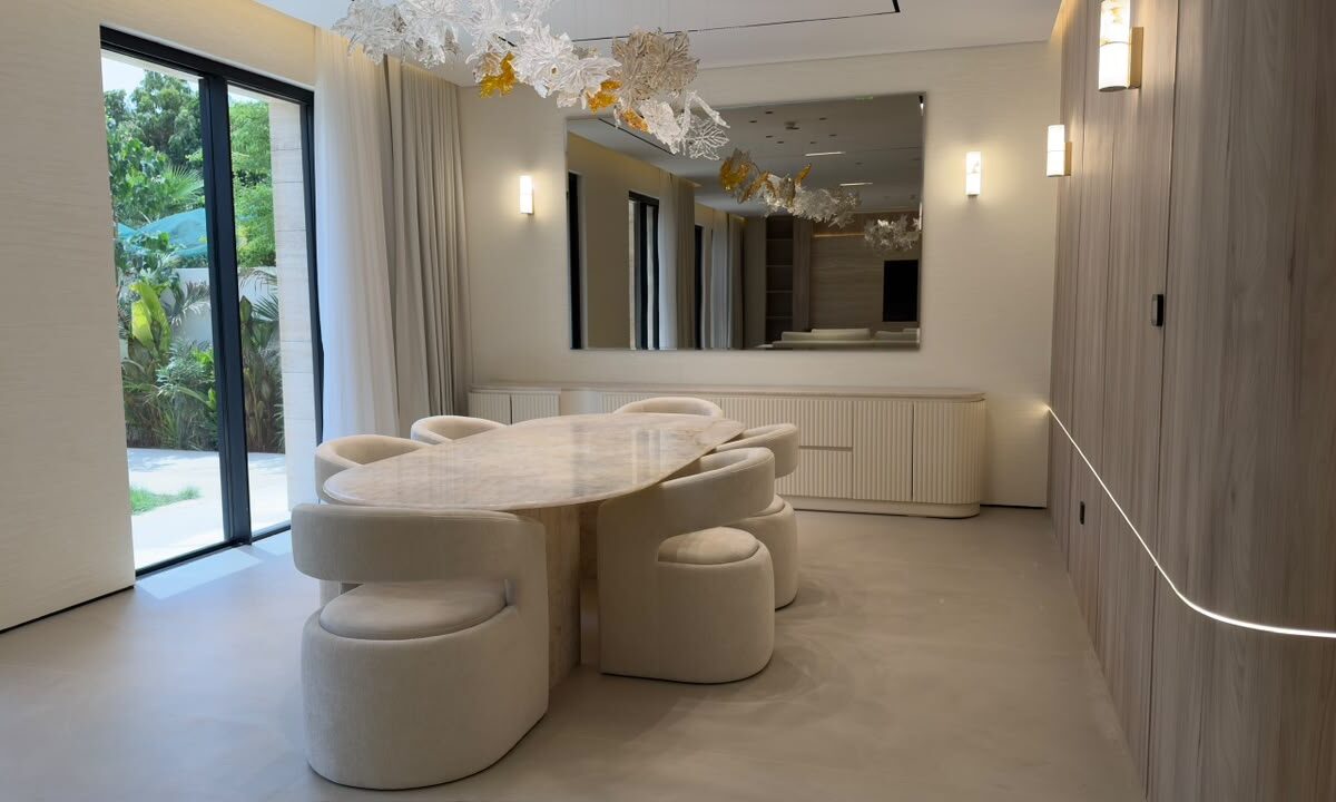 Dining room of a private villa at Wild Flower, Jumeirah Golf Estates — oval stone table, bouclé chairs, glass-leaf chandelier and garden doors