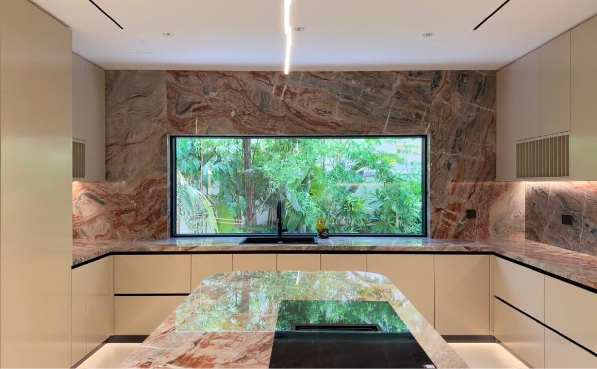 Turnkey villa kitchen in Jumeirah Golf Estates, Dubai — dramatic veined stone island and breakfast bar with garden window
