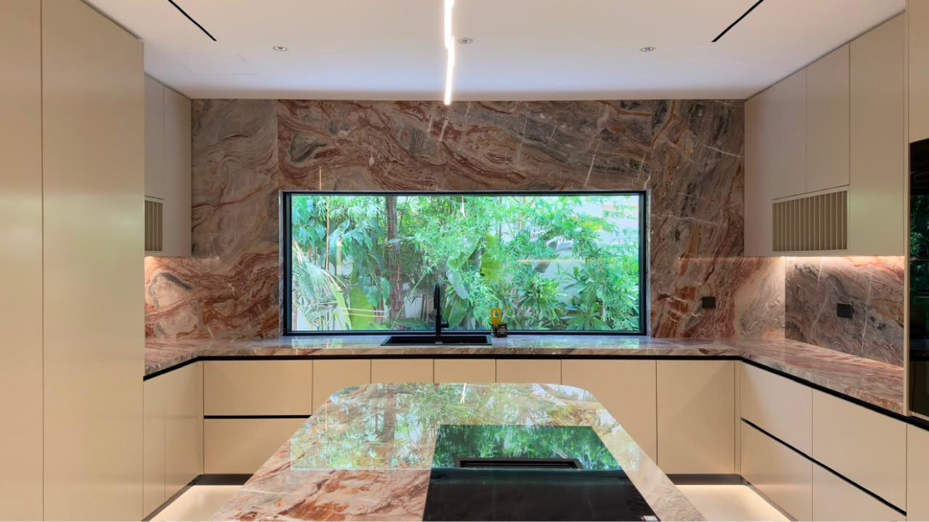 Turnkey villa kitchen in Jumeirah Golf Estates, Dubai — dramatic veined stone island and breakfast bar with garden window
