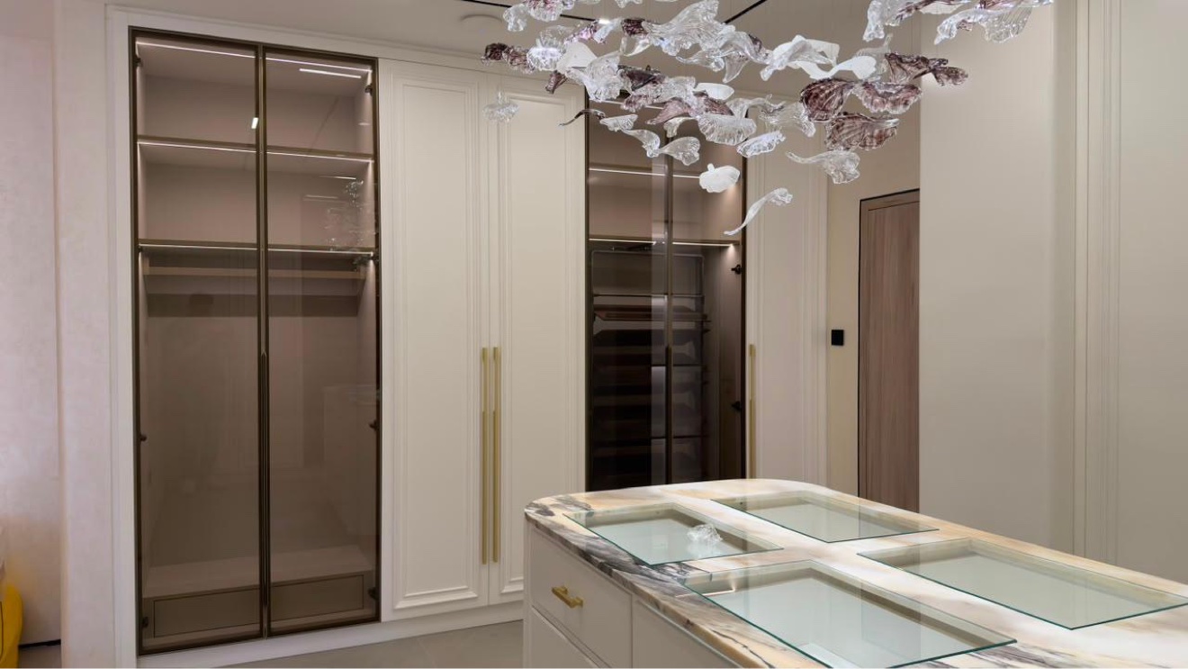 Walk-in wardrobe with glass-fronted cabinets and illuminated island drawers